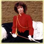 A woman in a red blouse holding a riding crop, sitting on a couch.