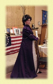 Woman dressed in a historical costume holding a candle indoors.