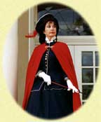 Woman in a vintage outfit with red cape and black hat.