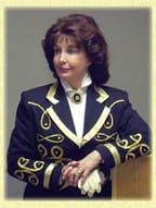 Woman in a formal black jacket with gold embroidery and white gloves.