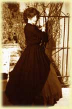 A woman in a vintage black dress stands by a wrought iron gate.